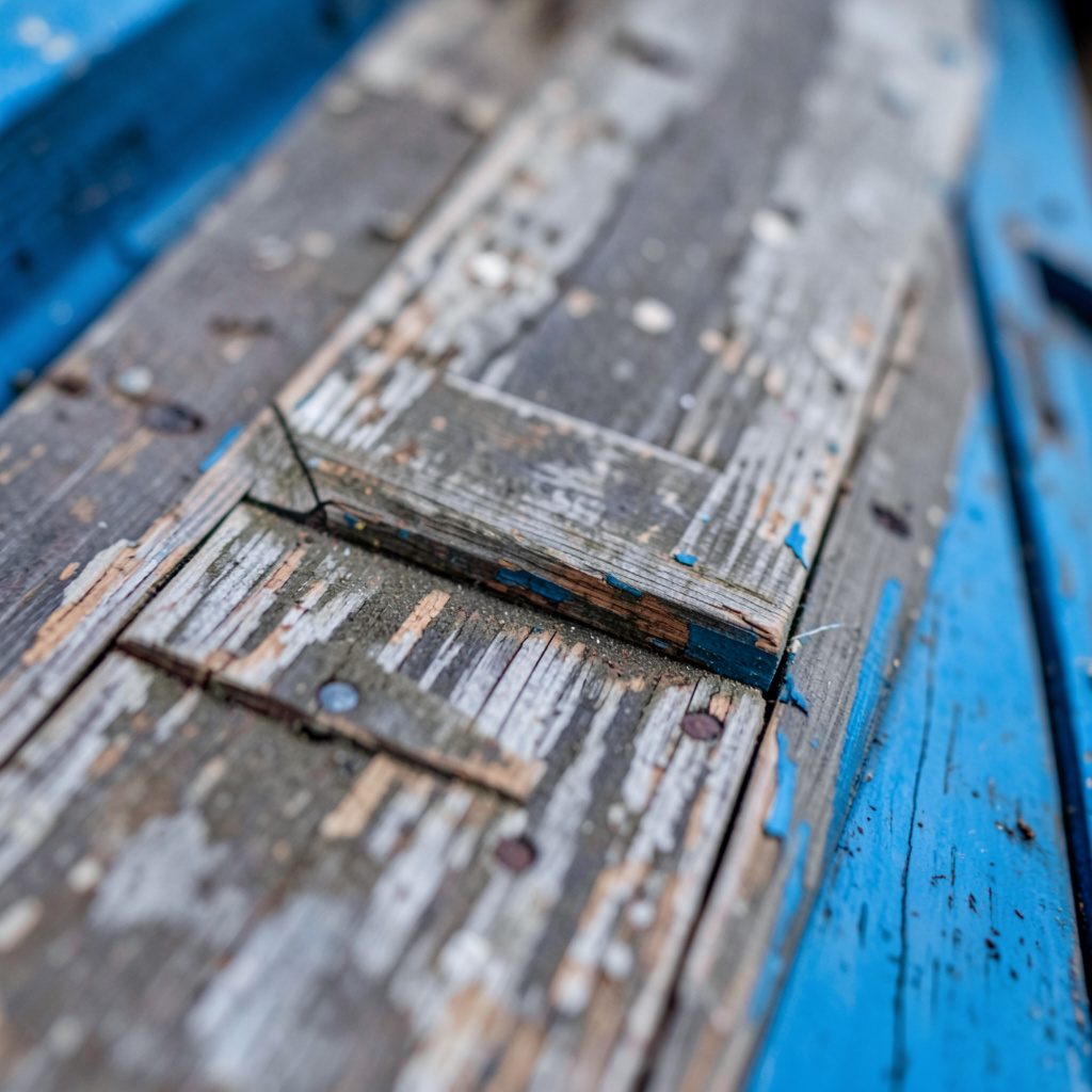 Close-up of weathered wooden planks on a historic storefront, muted gray-brown tones with peeling paint texture