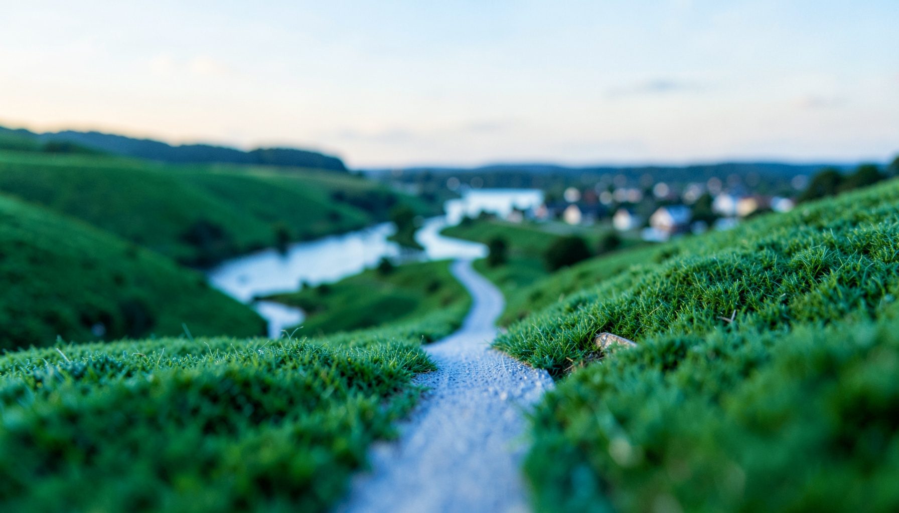 Rolling green hills along the Ohio River under a soft morning sky, with a narrow winding road leading toward a small riverside town in the distance